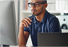 Person holding pen to mouth looking at computer screen with with ponderous look