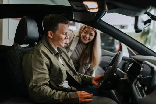 Man sitting in drivers seat of car smiling with salesperson standing in open door