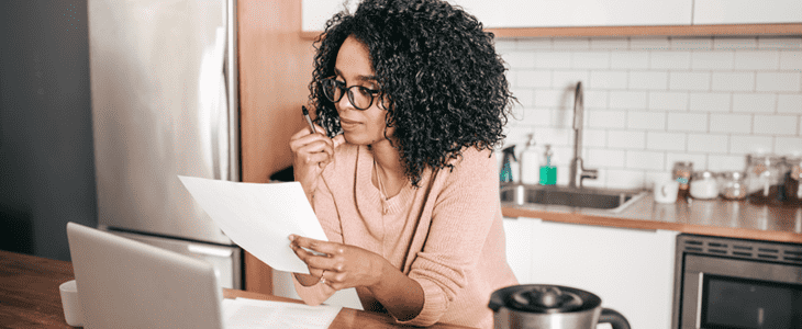 A woman reviewing a document at her laptop in a kitchen.