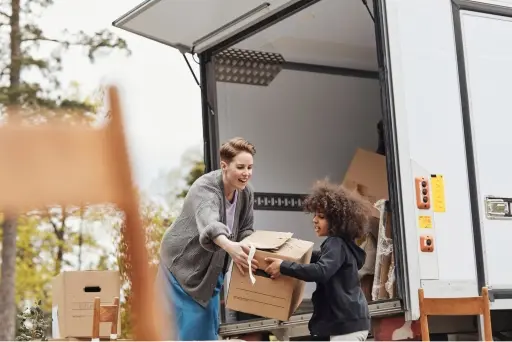 An adult helping a child take a box out of a moving truck