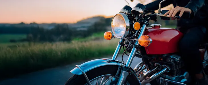 A person rides a classic red motorcycle down a scenic country road at sunset.