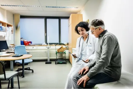 A doctor sitting down with a male patient in a medical office going over the patients chart