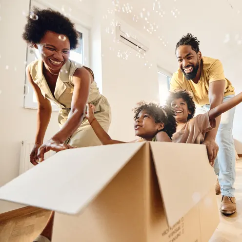 Family playing with 2 kids sitting in moving box while parents push