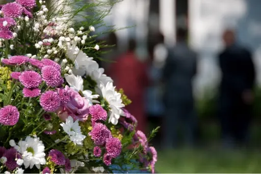 Flower arrangement at funeral with blurred images of people in the background