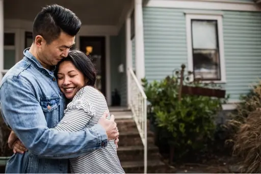 Middle aged couple hugging outside of home near the front steps