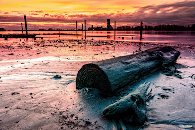 Golden hour hues paint the sky as a lone log rests on the river's edge