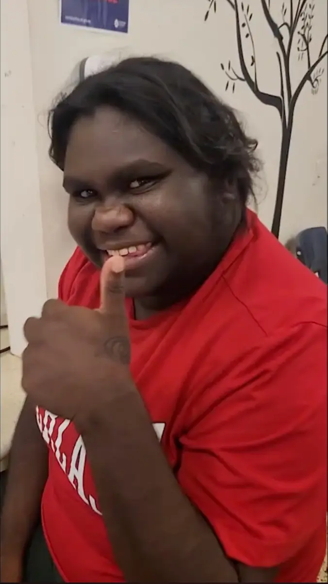 A person smiles broadly and gives a thumbs-up gesture while wearing a bright red t-shirt.