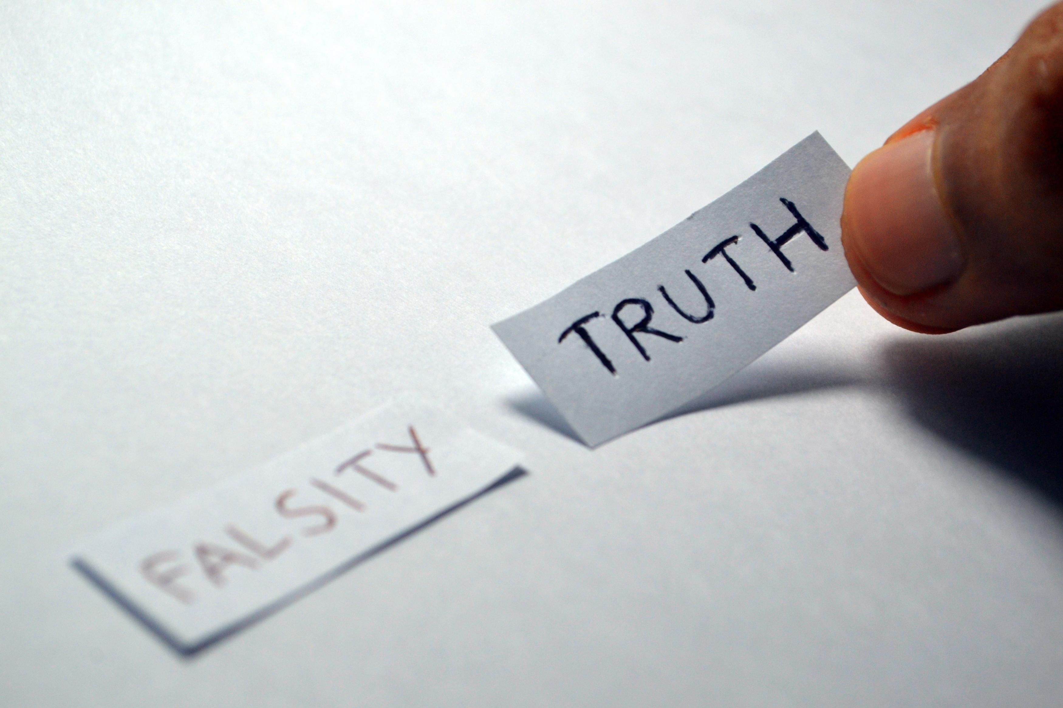 Hand placing paper stating “truth” beside paper stating “falsity” on a white background.