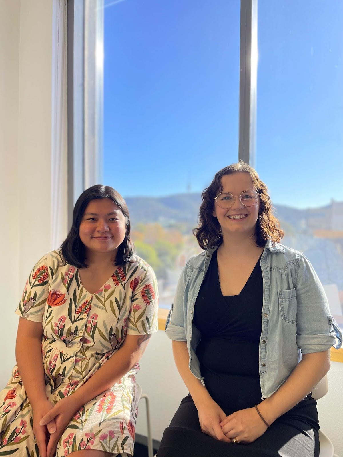 LewChing Yip and Cate sitting next to each other in front of a window