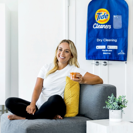 Woman sitting on a sofa with a Tide Cleaners dry cleaning bag in the background