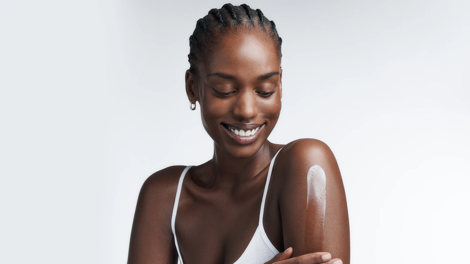 Frau trägt Körperpflege-Creme auf den Arm auf und lächelt, Nahaufnahme mit hydratisierter Haut.