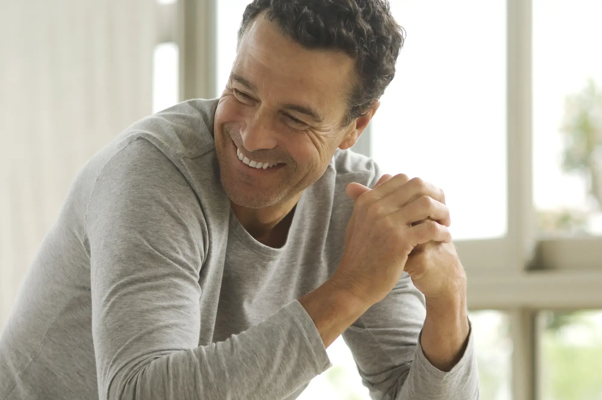 Ein lächelnder mann mittleren Alters, der seine Hände zusammen faltet.