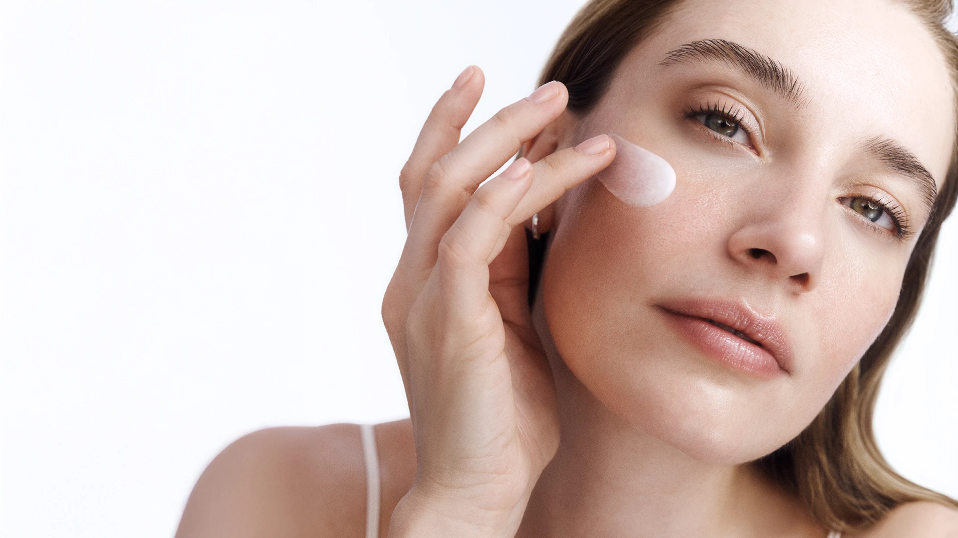 Frau trägt sanft Gesichtspflege-Creme auf die Wange auf, Nahaufnahme für Hautpflege und Beauty-Routine