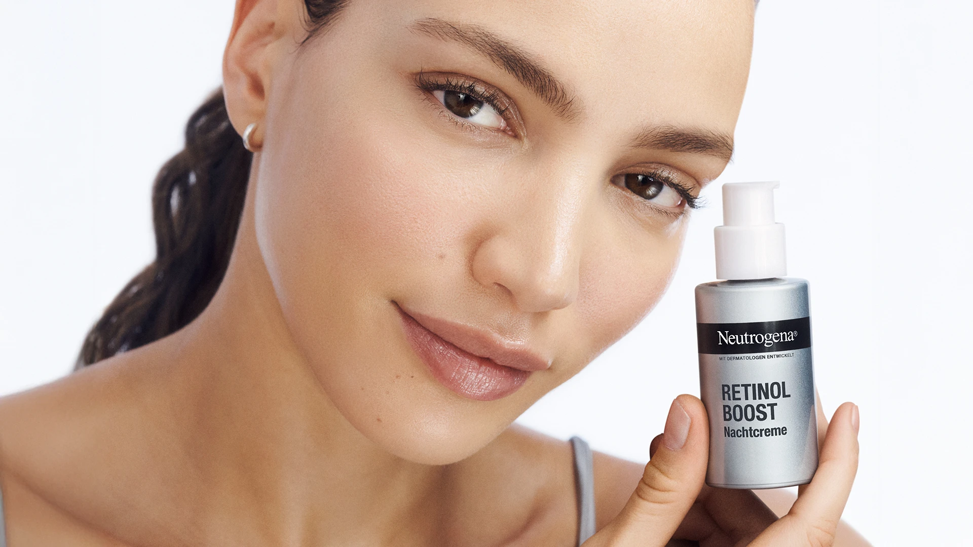 Frau hält Neutrogena Retinol Boost Nachtcreme für Anti-Age Gesichtspflege in der Hand, Nahaufnahme mit natürlicher Haut.