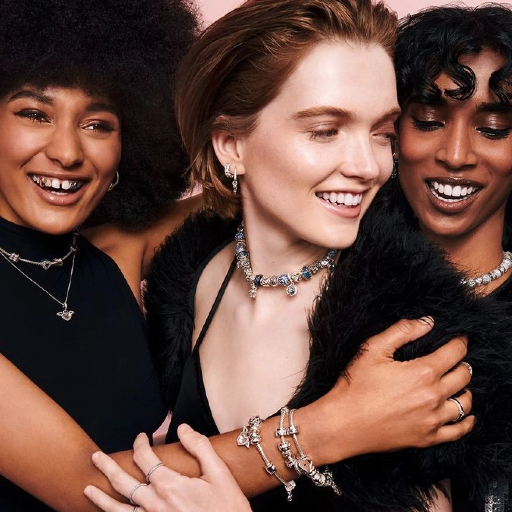 Three diverse young women hugging and smiling, wearing all black and decked out in silver bedazzled jewelry