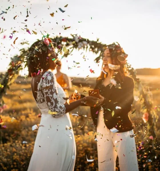 A Black woman and a White woman celebrate at an outdoor wedding in a field