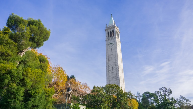 Historic tower framed by green and yellow trees against a blue sky.