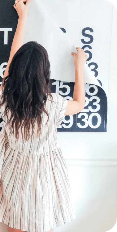 woman affixing a large calendar to a wall 