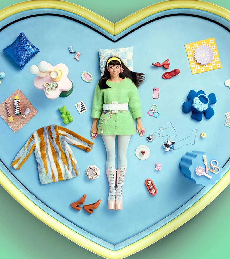 A woman lying on the floor surrounded by colorful, vintage-inspired accessories, clothing and home decor