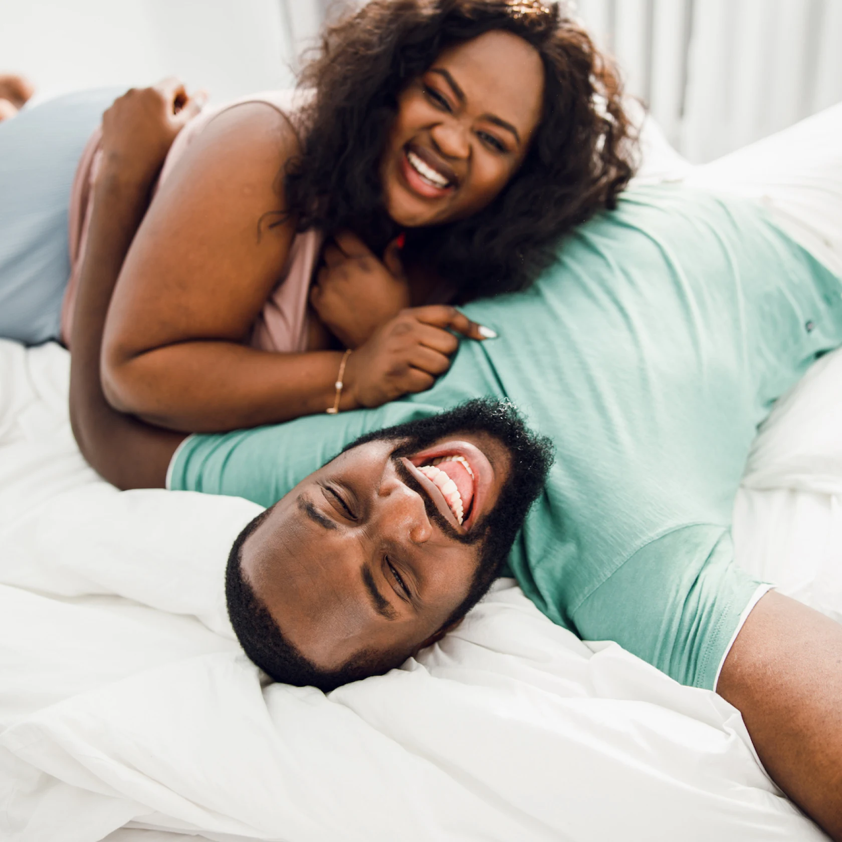 Smiling black couple laying together on white bedsheets. 