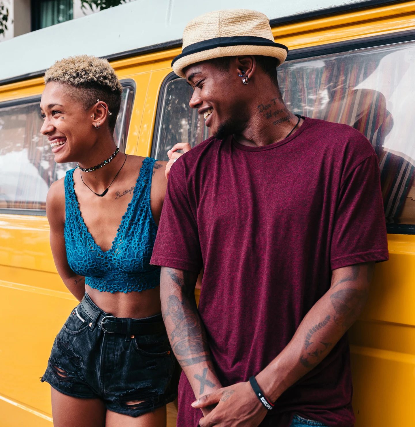 A Black man and Black woman smiling and leaning against a yellow car.