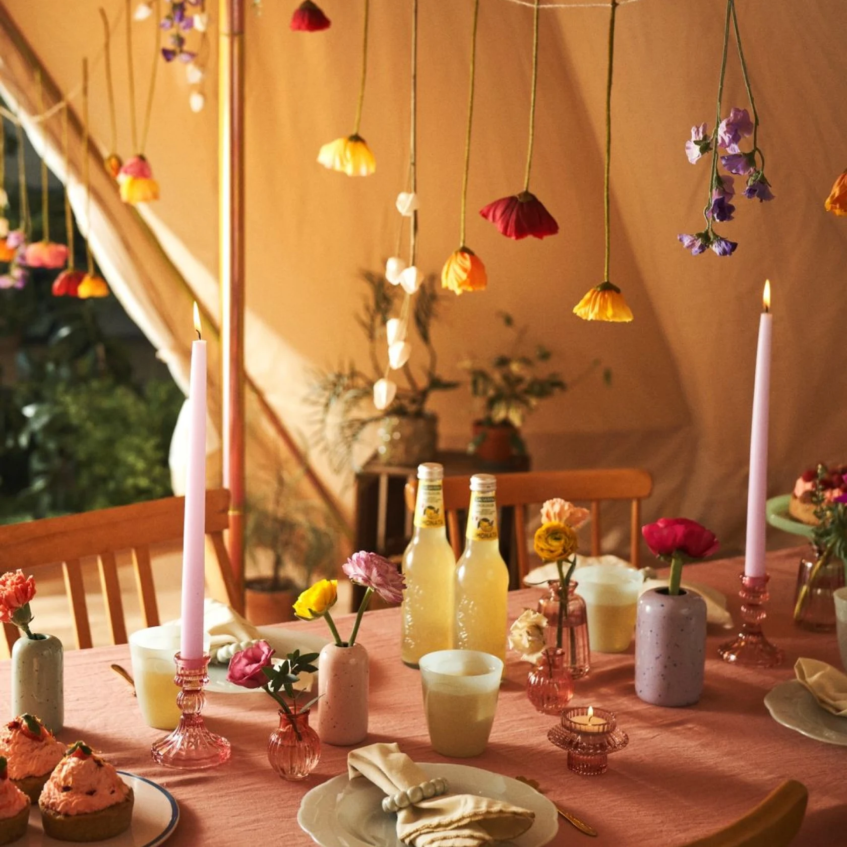 Gedeckter Tisch mit Blumen in Vasen und von der Decke hängend, pastellfarbene Deko und Desserts sowie elegantes Keramikgeschirr 