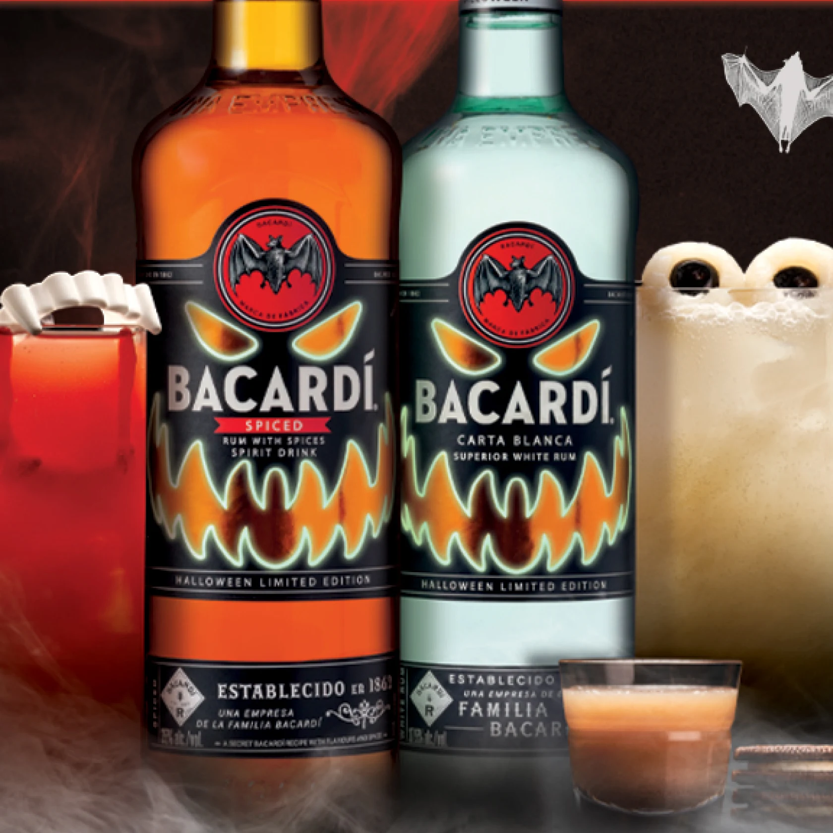 Two cocktails and two bottles of Bacardi are surrounded by smoke and Halloween bats 
