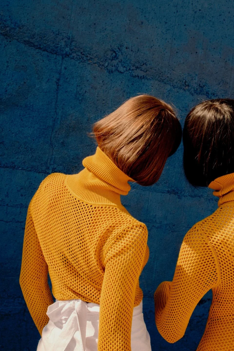 Dos mujeres de cabello corto y castaño que visten suéteres de cuello de tortuga color naranja.