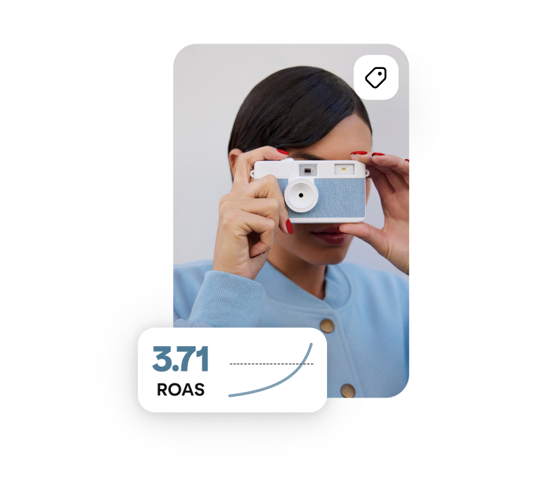 Una persona tiene in mano una fotocamera azzurra, con il testo "3.71 ROAS" sovrapposto nell'angolo. 