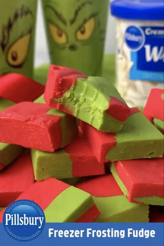Pin showing Grinch-themed fudge pieces stacked in a pile with Pillsbury logo and title of recipe “Freezer Frosting Fudge” running along the bottom of image.