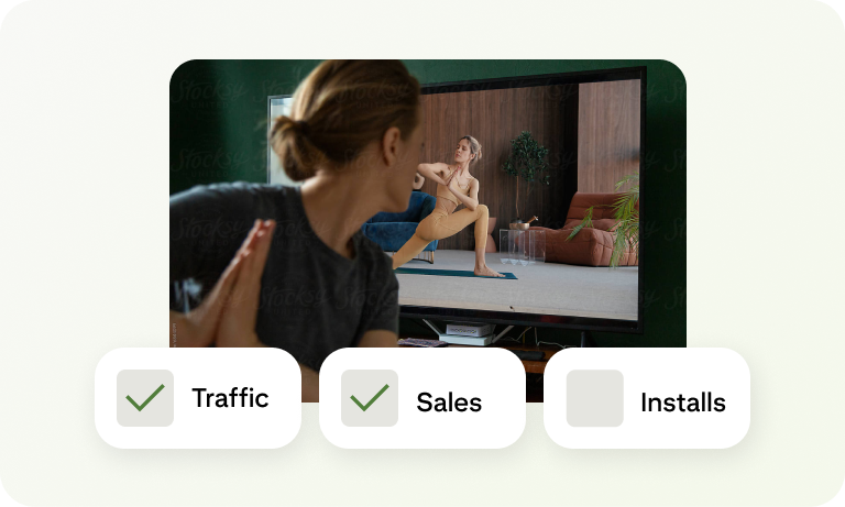 A woman watching a fitness video on a TV screen, with  campaign goals labeled Traffic, Sales, and Installs below.