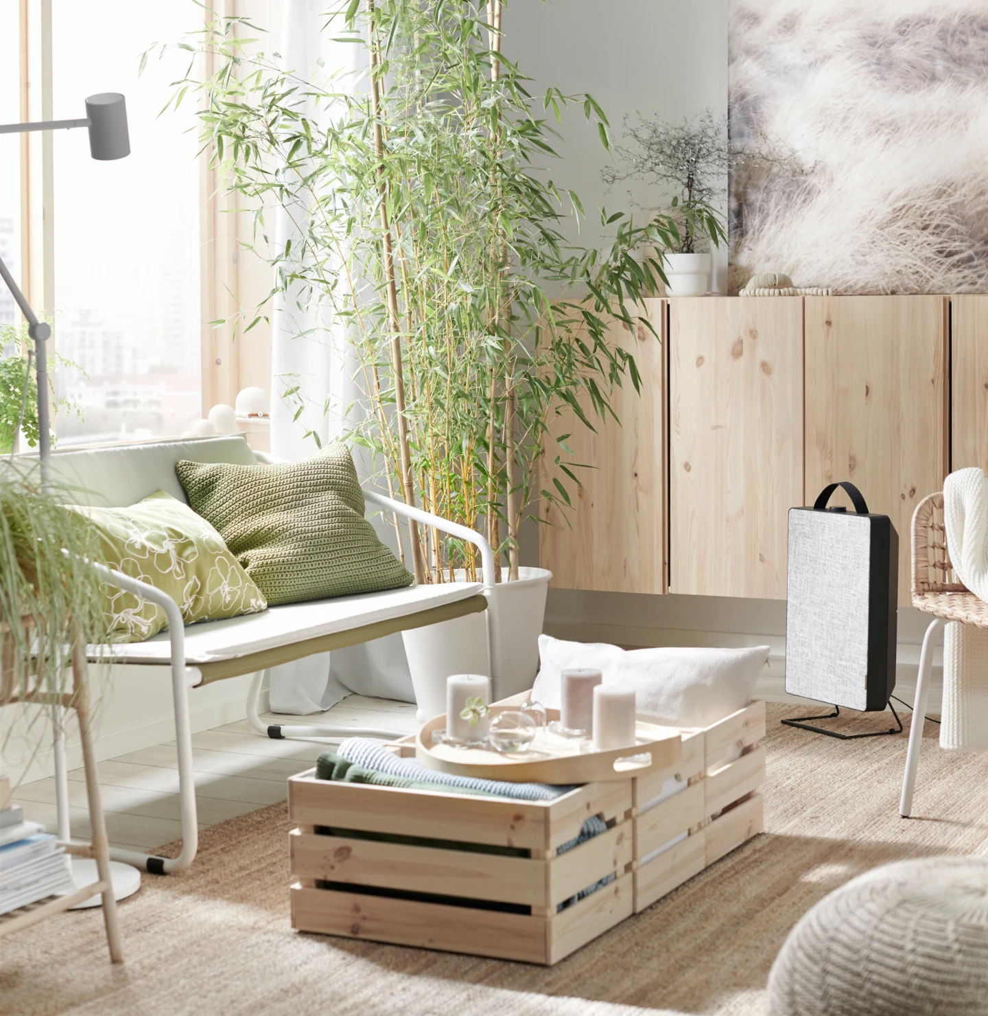 Bright living room setting with a white love seat with green pillows, bamboo plant and unfinished wood table and cabinets