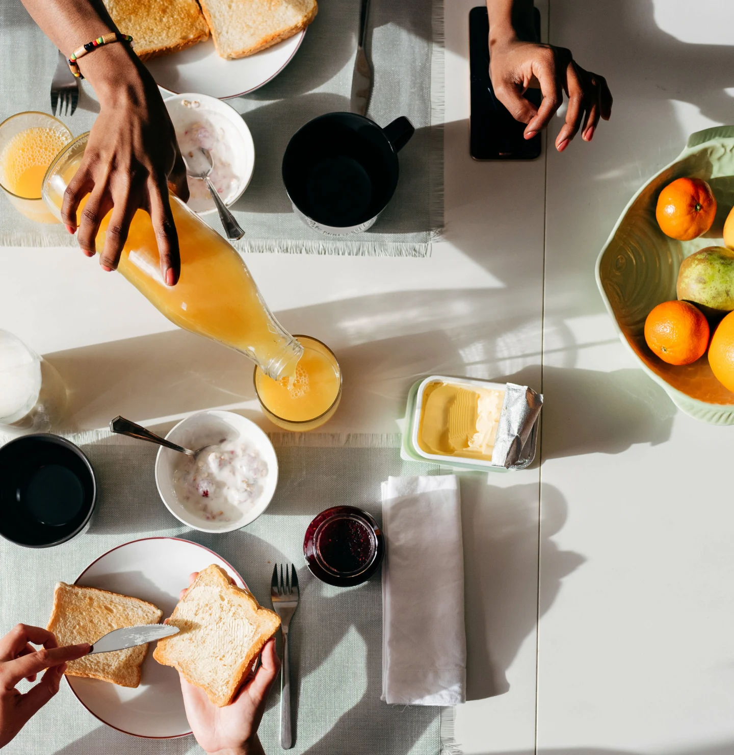 Overhead view of a breakfast table with hands pouring juice and buttering toast