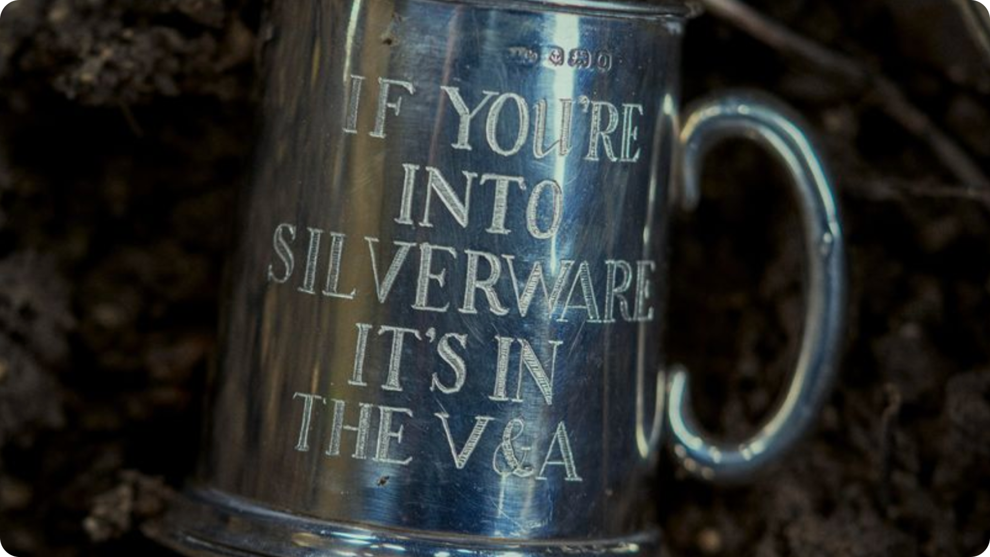 A silver mug lying on the ground is etched with the words,“If you’re into silverware it’s in the V&A”.