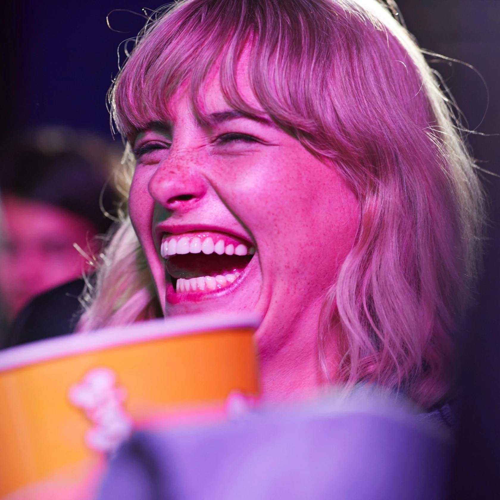 Mulher rindo no cinema com um grande balde de pipoca