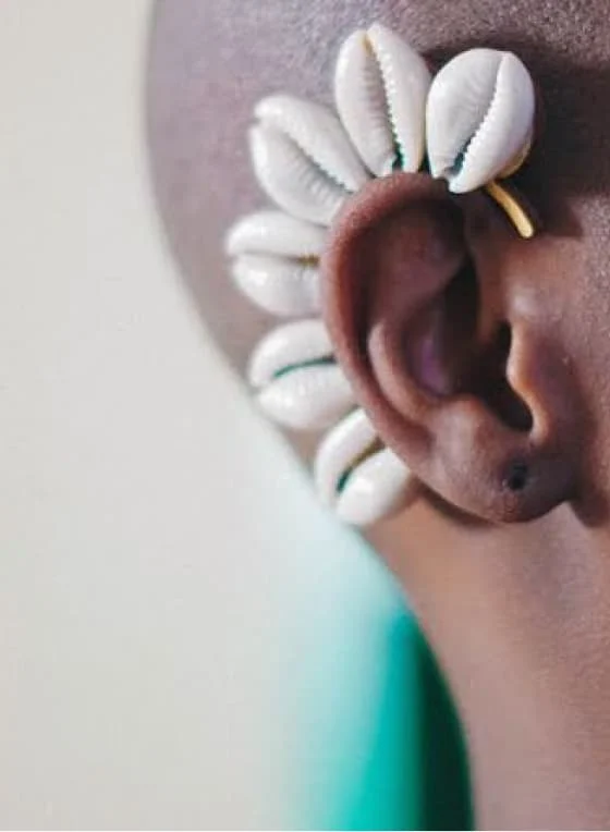 A Pin featuring a closeup of a cowrie cluster ear cuff from Draped, on a Black female model.