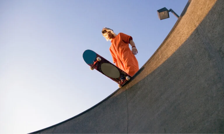 Person in orange jumpsuit with skateboard at the top of a half-pipe