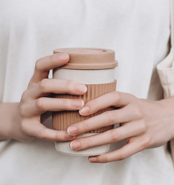 White hands hold a recyclable to-go coffee cup