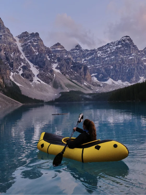 Una mujer blanca en un kayak amarillo con montañas en la distancia