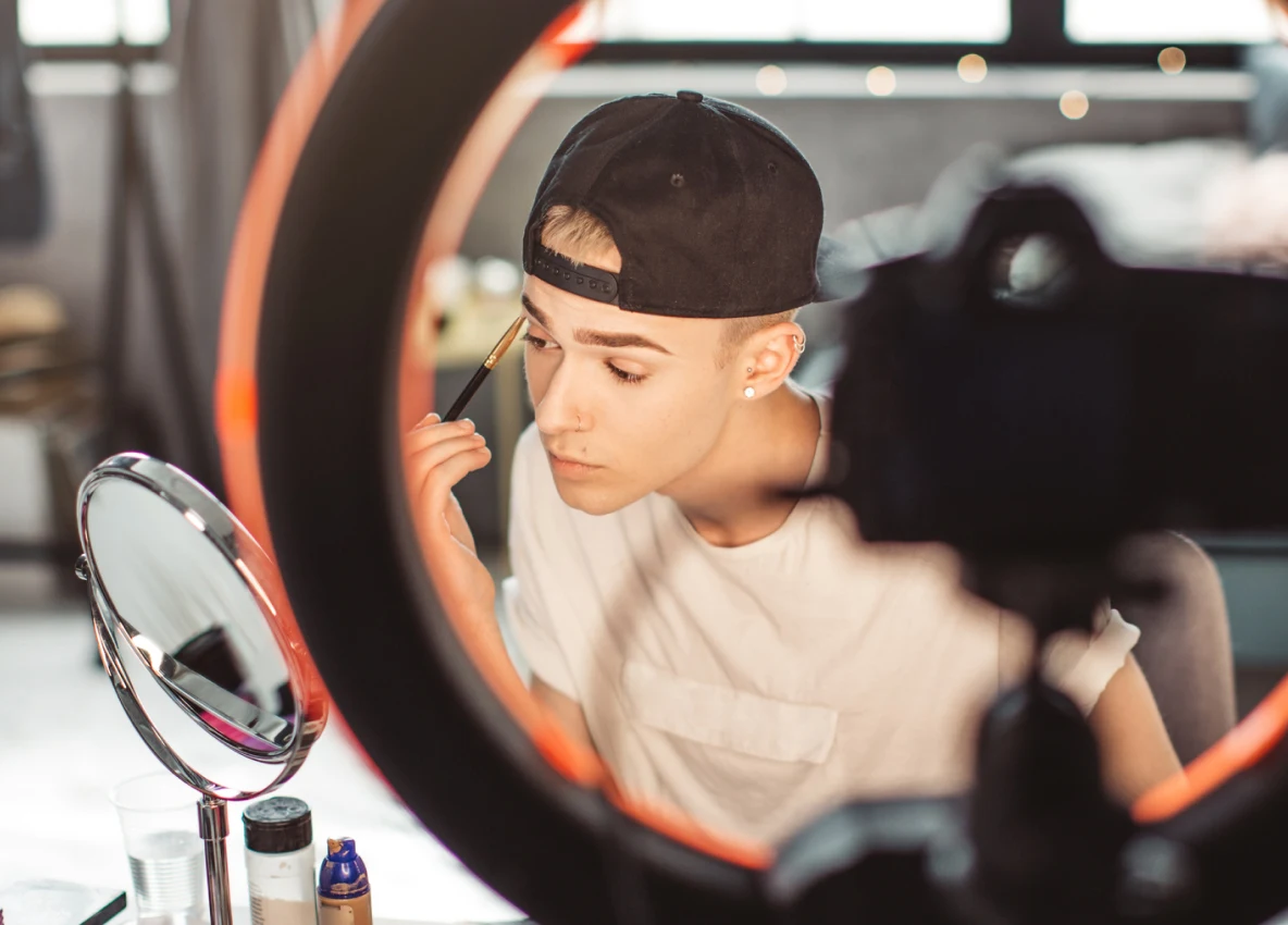 Man applying eye makeup in a mirror in front of a ring light. 