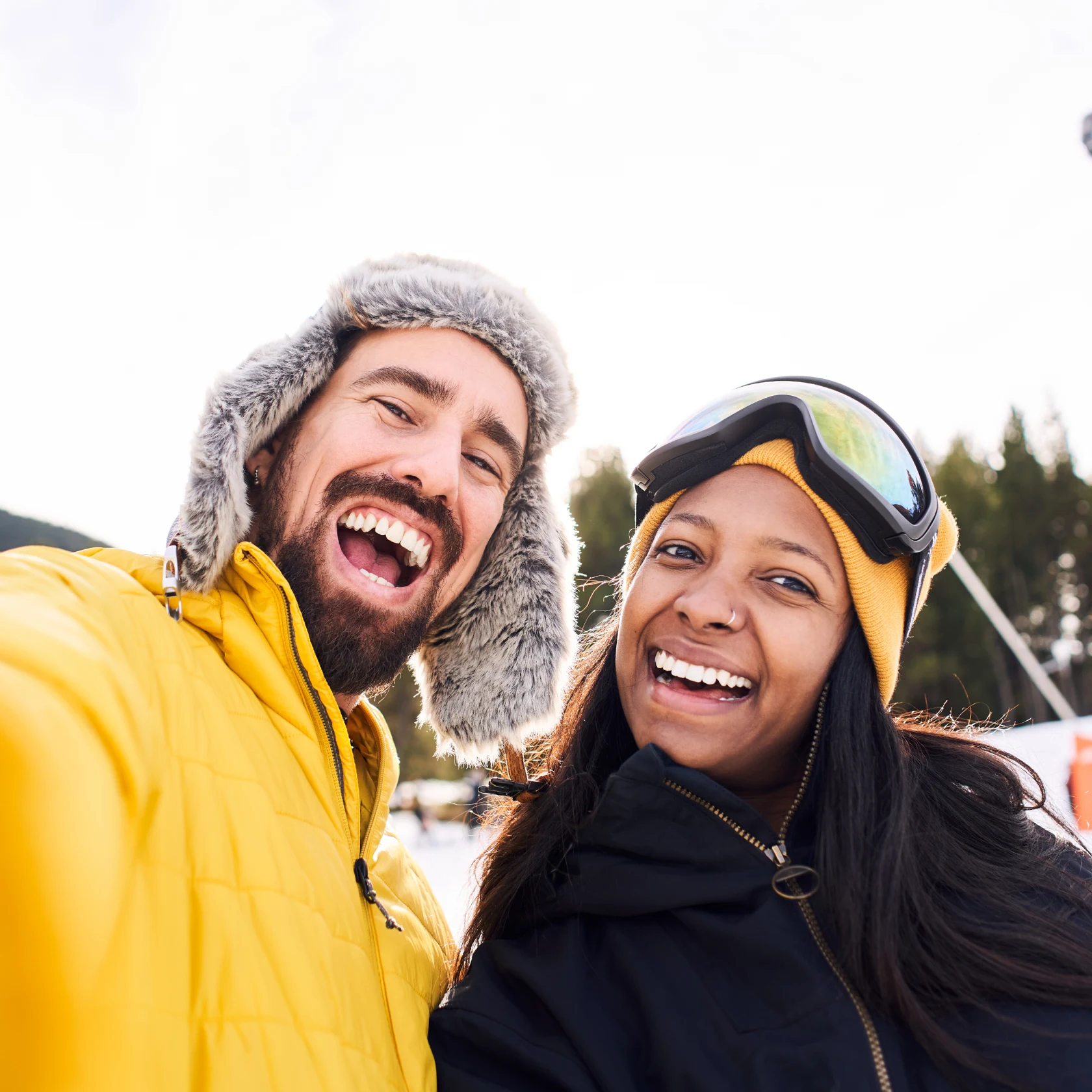 Junge Männer und Frauen lächeln in die Kamera, draußen im Schnee, mit Mützen für kaltes Wetter und dicken Jacken
