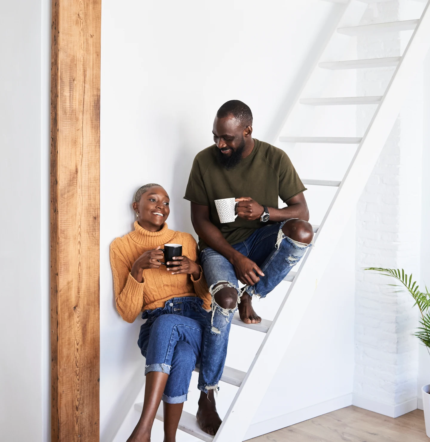 Hip Black woman and man with mugs sitting on a white staircase