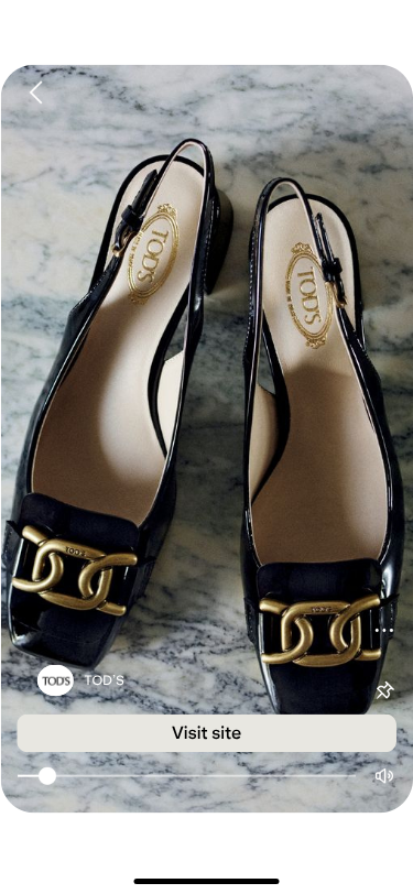A pair of elegant black Tod's slingback shoes with gold chain accents on a gray marble surface, conveying luxury and sophistication.