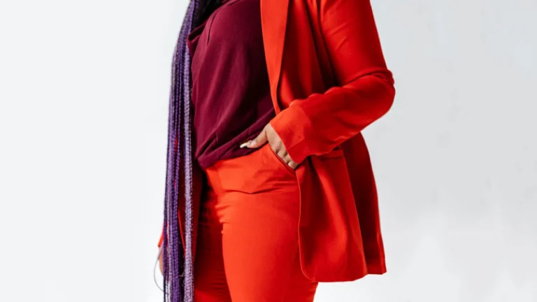 A focused shot of a woman wearing a bright orange pant suit with a maroon shirt and purple scarf accessory.