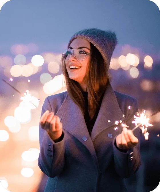 a smiling White woman in an overcoat holding sparklers