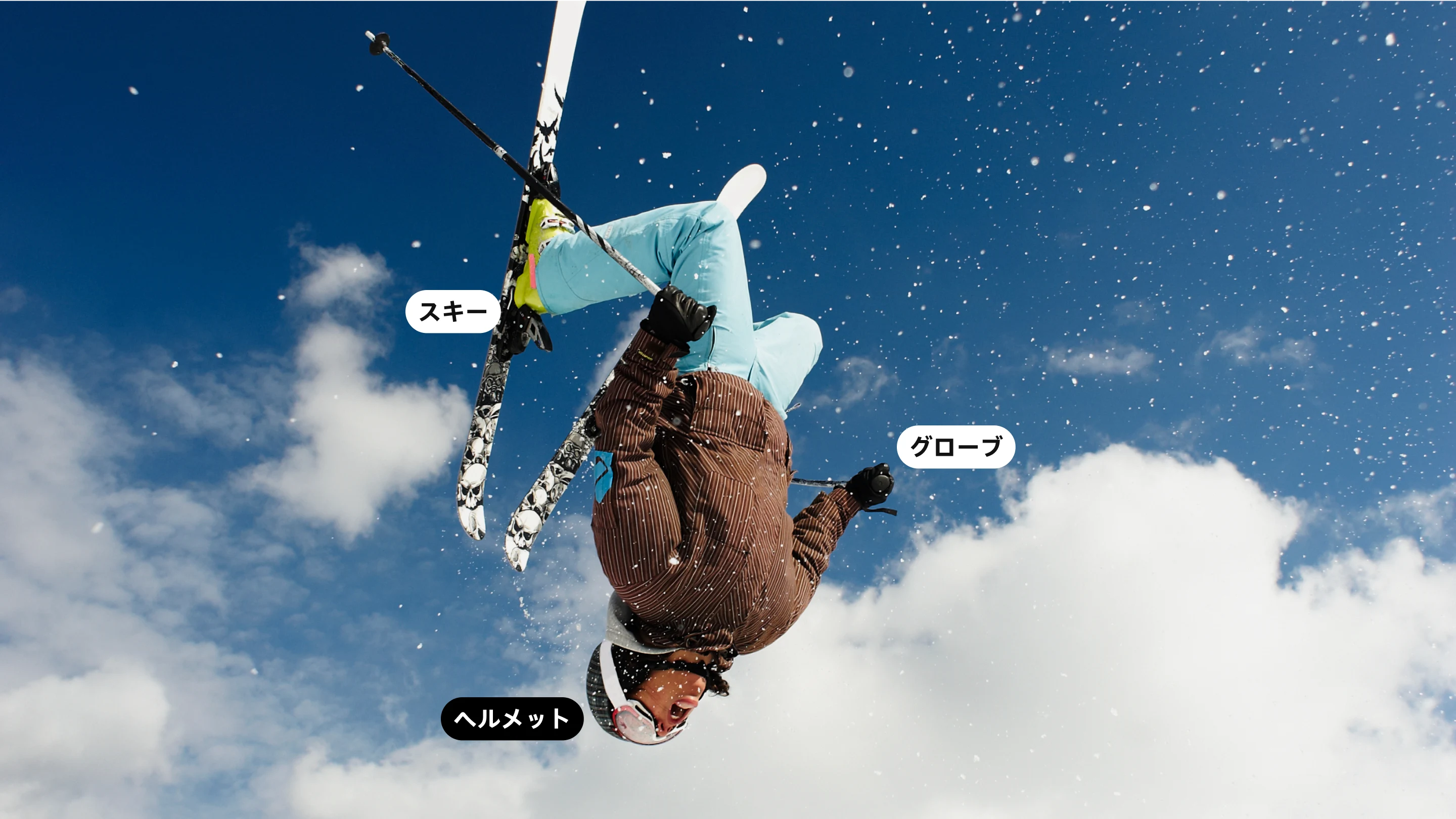 スキーウェアを着てスキーを履き、空中で一回転している女性の姿を捉えたフル画面の画像。