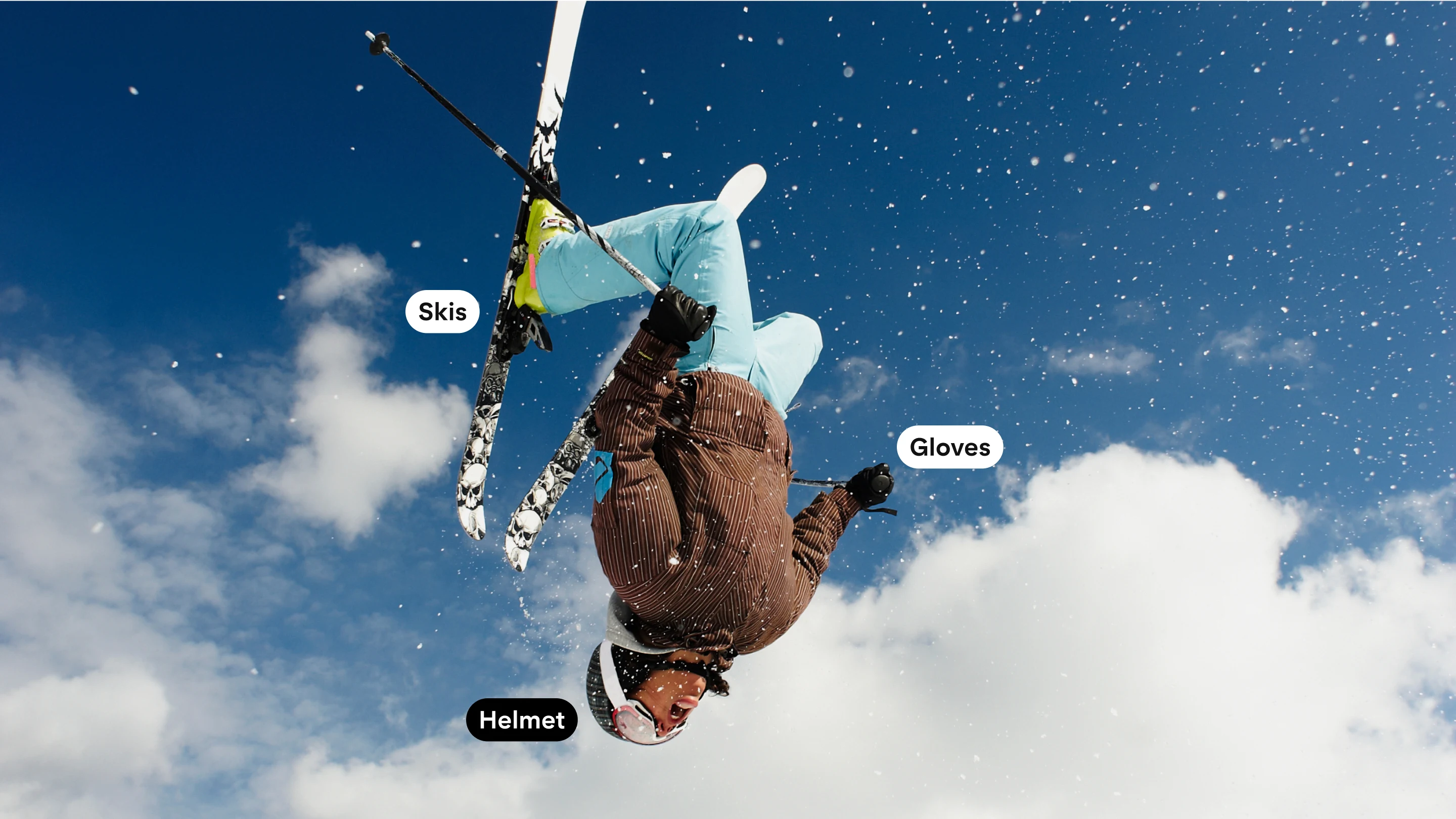 Full width image featuring a woman flipping upside down in full snow gear and skis.