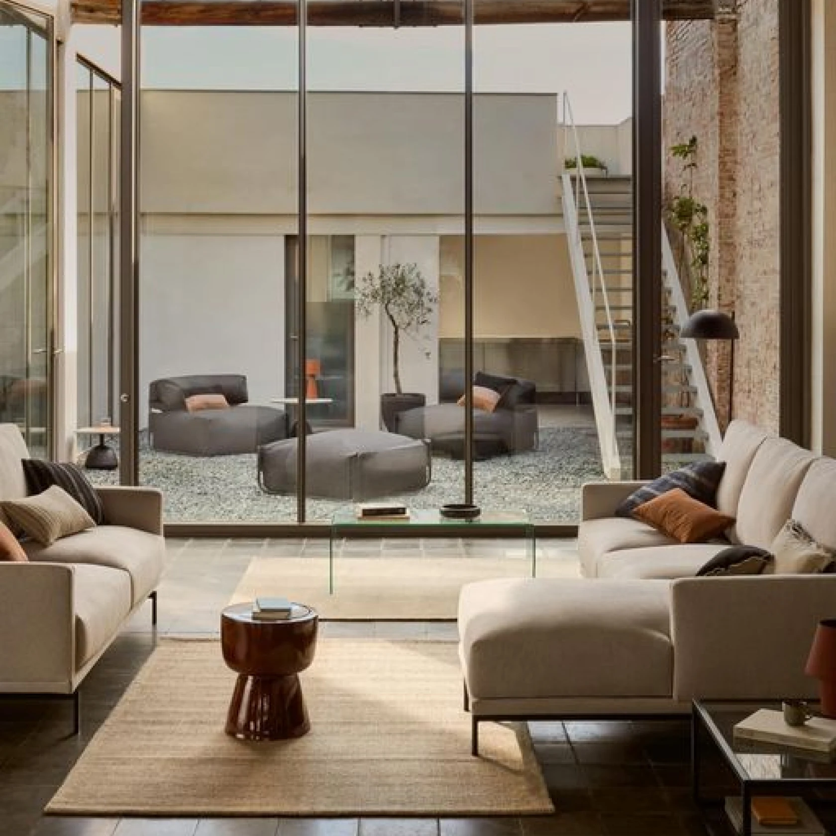Sala de estar con sofás crema mirando a través de ventanas de piso a techo hacia el patio con muebles de descanso al aire libre