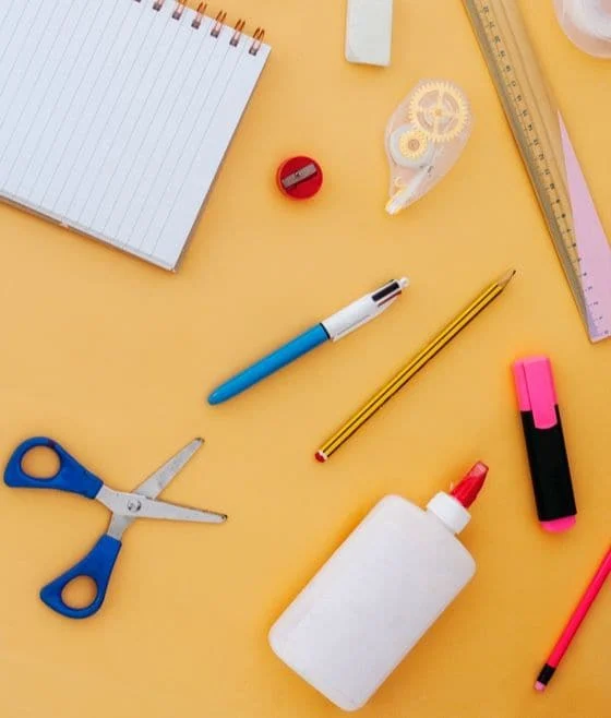 Material escolar disposto sobre uma mesa amarela com o slogan "Faça um estoque de itens essenciais para a volta às aulas"
