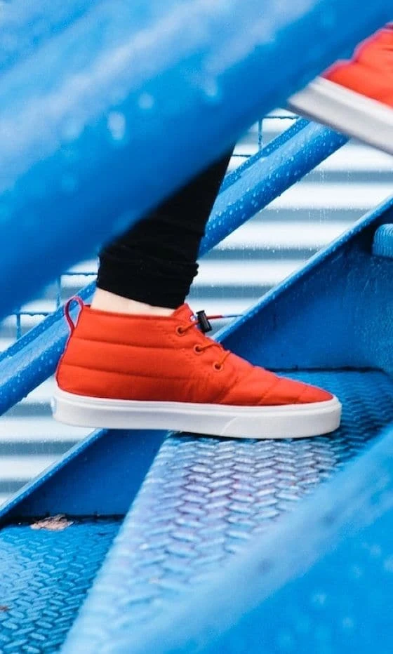 Persona che sale delle scale blu con delle sneakers rosse alla caviglia